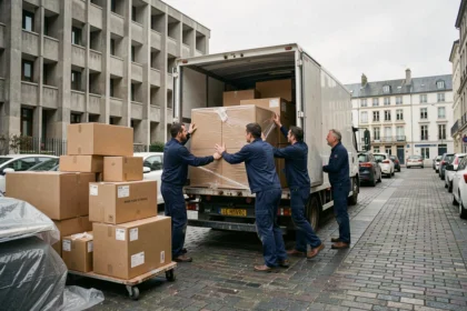 Équipe de déménageurs professionnels chargeant un camion devant un immeuble havrais en béton, avec cartons et meubles protégés sur le trottoir